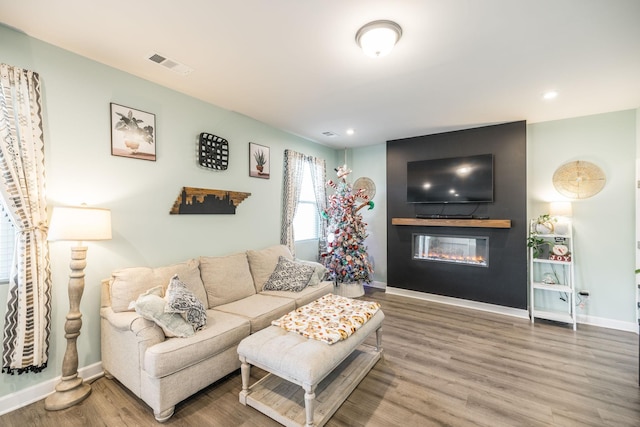 living area with recessed lighting, visible vents, a glass covered fireplace, wood finished floors, and baseboards