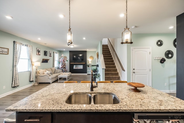 kitchen featuring open floor plan, dishwasher, a glass covered fireplace, a center island with sink, and pendant lighting