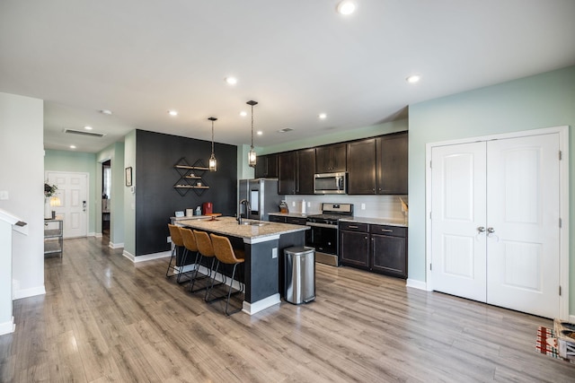 kitchen featuring light wood-type flooring, a kitchen bar, appliances with stainless steel finishes, and dark brown cabinets