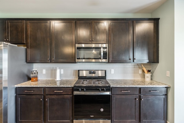 kitchen with stainless steel appliances, dark brown cabinets, backsplash, and light stone counters