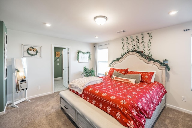 carpeted bedroom featuring ensuite bathroom, visible vents, and baseboards