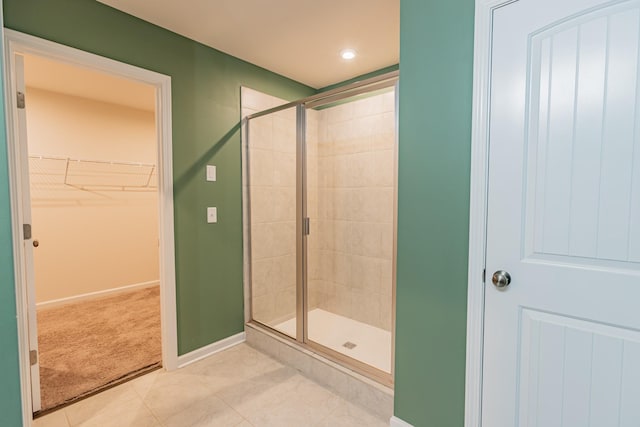 bathroom featuring a stall shower, tile patterned flooring, a walk in closet, and baseboards