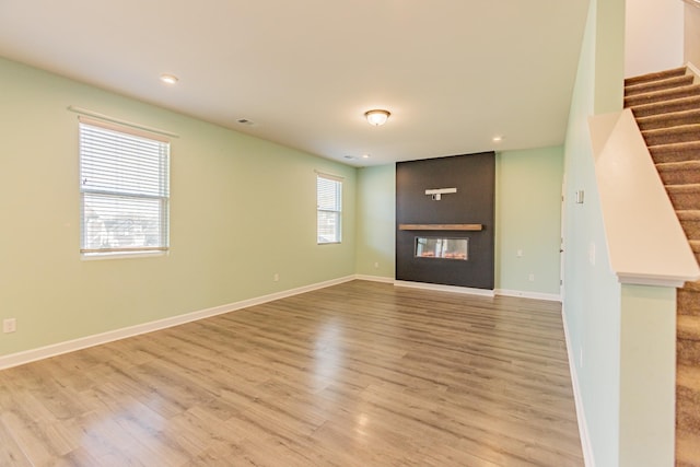 unfurnished living room with stairway, a fireplace, wood finished floors, and baseboards