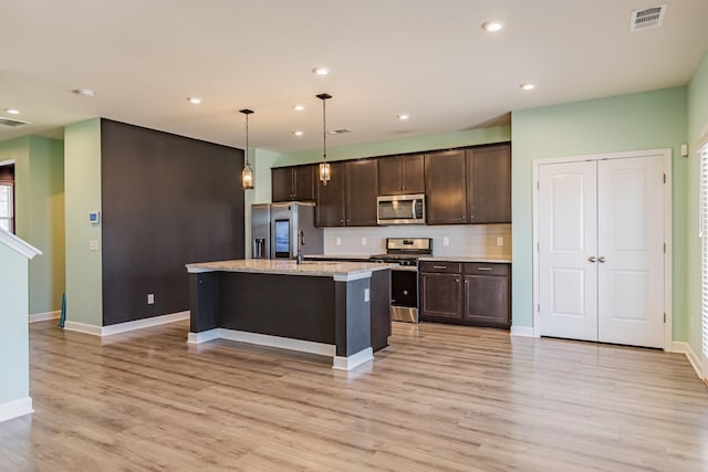 kitchen featuring a kitchen island with sink, light wood-style flooring, visible vents, dark brown cabinets, and appliances with stainless steel finishes