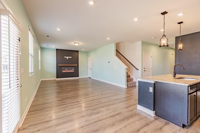 kitchen with a glass covered fireplace, light wood-style flooring, light stone countertops, a sink, and recessed lighting