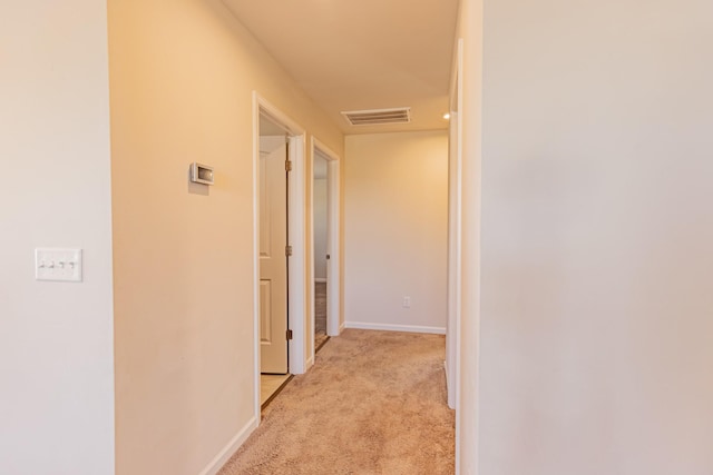 hall with baseboards, visible vents, and light colored carpet