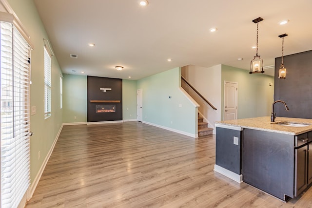 kitchen with a large fireplace, baseboards, light wood-type flooring, a sink, and recessed lighting