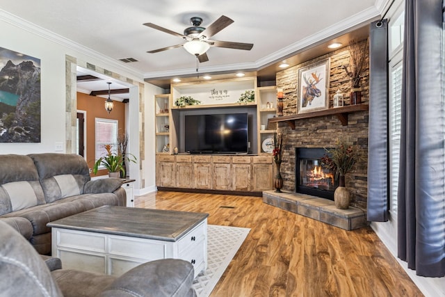 living room featuring visible vents, light wood-style flooring, ceiling fan, ornamental molding, and a stone fireplace