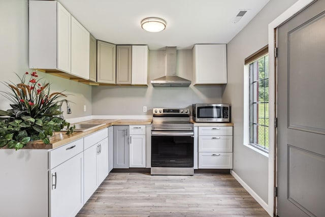 kitchen with a wealth of natural light, light countertops, appliances with stainless steel finishes, a sink, and wall chimney range hood