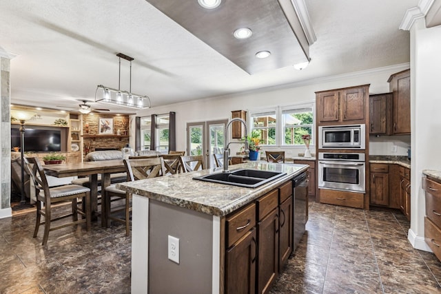 kitchen featuring stainless steel appliances, a kitchen island with sink, a sink, and light stone counters