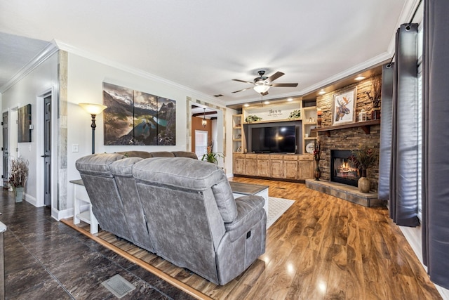 living room featuring ceiling fan, a stone fireplace, built in features, baseboards, and ornamental molding