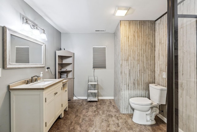 bathroom with toilet, wooden walls, vanity, visible vents, and baseboards