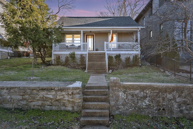 bungalow featuring central air condition unit, a shingled roof, covered porch, a lawn, and stairs