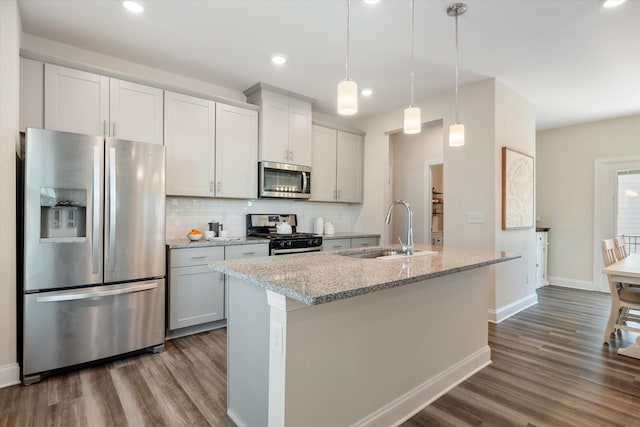 kitchen with light stone counters, decorative light fixtures, appliances with stainless steel finishes, a sink, and an island with sink