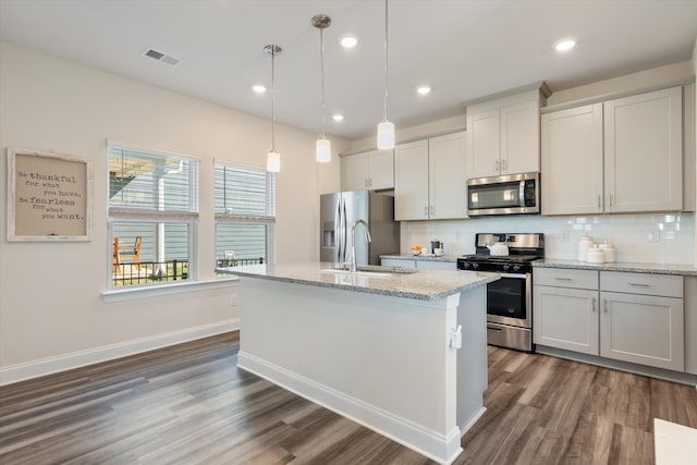 kitchen featuring visible vents, appliances with stainless steel finishes, decorative backsplash, a center island with sink, and pendant lighting