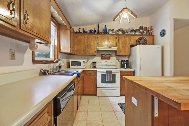 kitchen featuring white appliances, under cabinet range hood, brown cabinets, and a sink