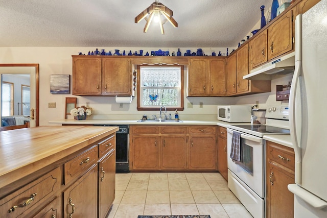 kitchen with brown cabinetry, white appliances, a sink, and under cabinet range hood