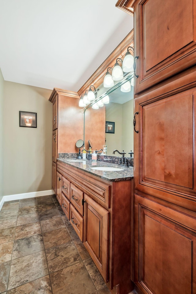 full bath featuring double vanity, stone finish flooring, baseboards, and a sink