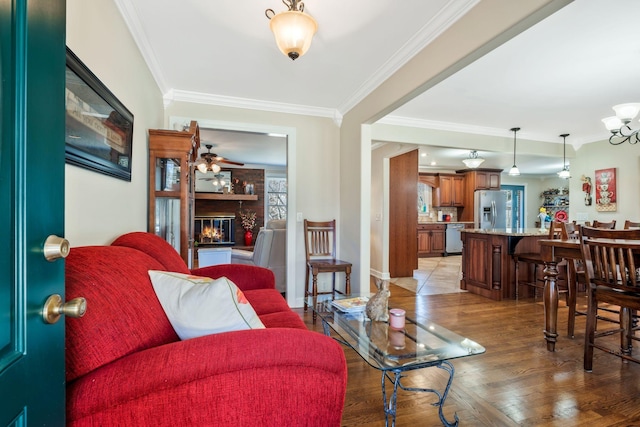 living area featuring a fireplace, a ceiling fan, baseboards, ornamental molding, and light wood finished floors