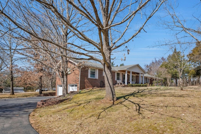 view of front of house featuring brick siding, a porch, a front yard, a garage, and driveway