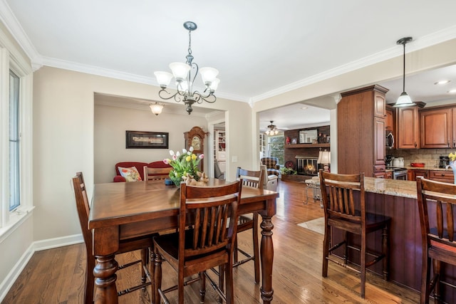 dining area with baseboards, ornamental molding, dark wood-type flooring, and a glass covered fireplace