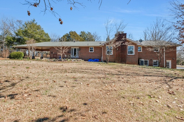 rear view of house featuring brick siding, a lawn, a chimney, and central air condition unit