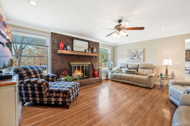 living area featuring crown molding, a brick fireplace, ceiling fan, wood finished floors, and baseboards