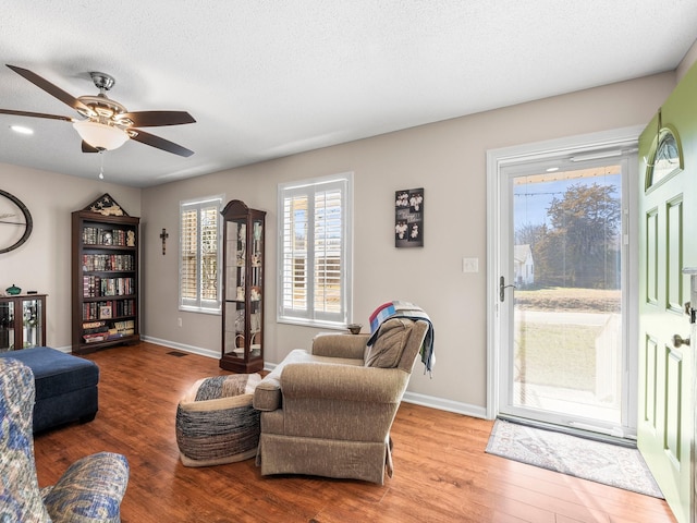 living area featuring visible vents, a textured ceiling, baseboards, and wood finished floors