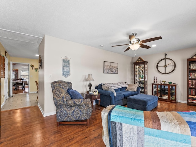 living area featuring attic access, ceiling fan, baseboards, and wood finished floors