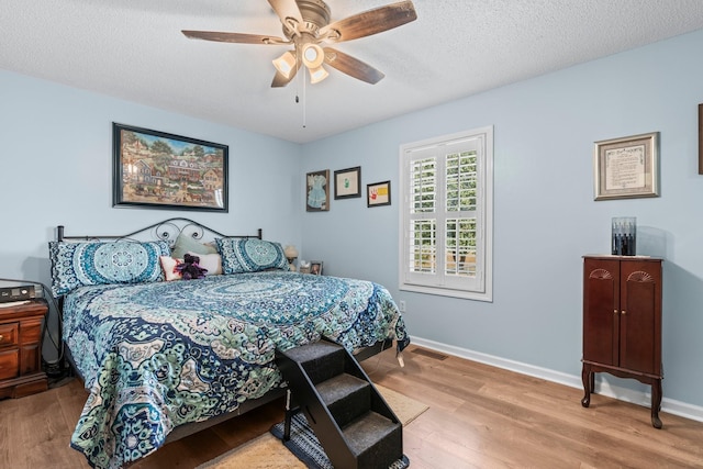 bedroom featuring baseboards, visible vents, ceiling fan, wood finished floors, and a textured ceiling