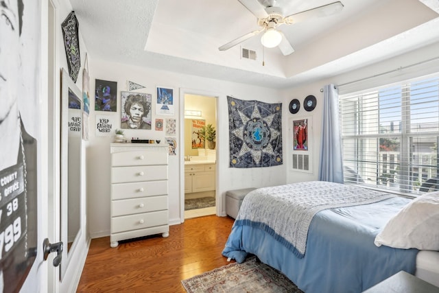 bedroom featuring connected bathroom, a ceiling fan, visible vents, dark wood-style floors, and a raised ceiling