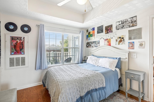 bedroom featuring ceiling fan, a raised ceiling, dark wood finished floors, and baseboards