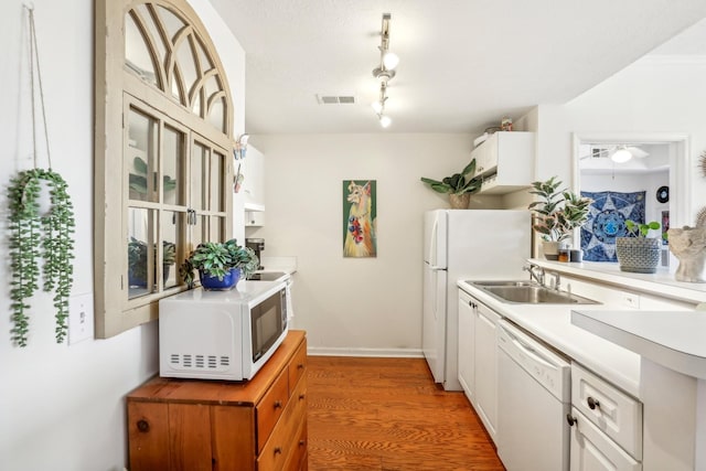 kitchen featuring white appliances, a sink, white cabinets, light countertops, and light wood-type flooring