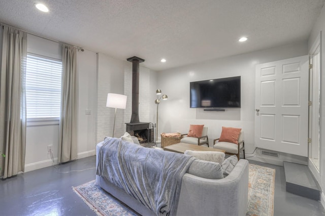 living area featuring recessed lighting, finished concrete floors, a wood stove, a textured ceiling, and baseboards