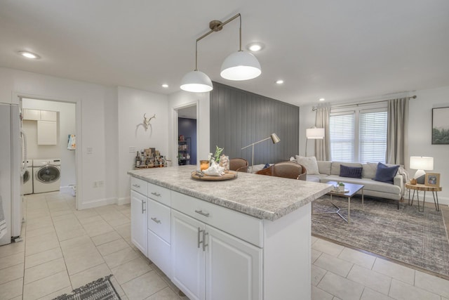 kitchen featuring washing machine and dryer, a kitchen island, white cabinetry, light countertops, and pendant lighting