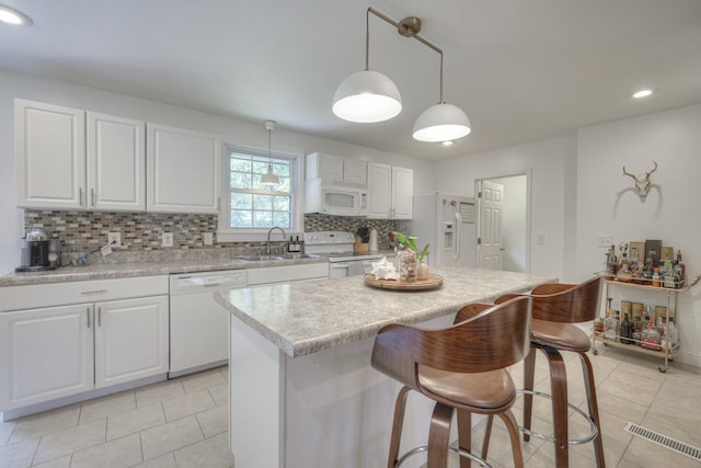 kitchen with light countertops, hanging light fixtures, white cabinets, a sink, and white appliances