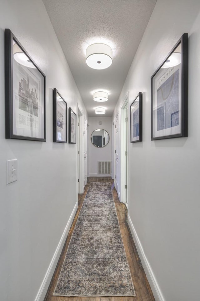 hallway with a textured ceiling, dark wood-style flooring, visible vents, and baseboards