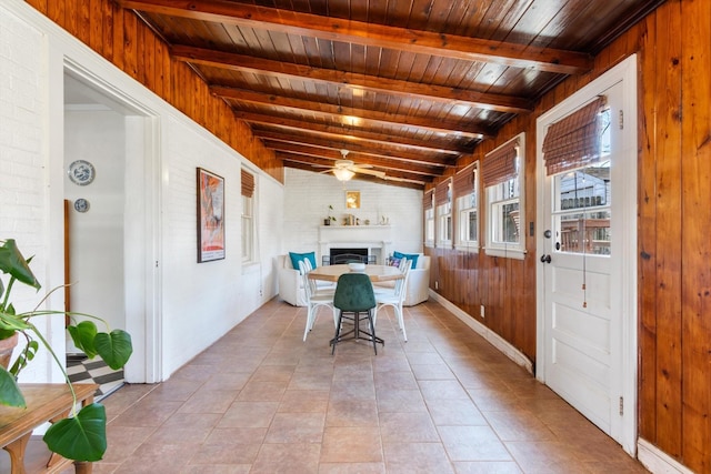 dining area with light tile patterned floors, lofted ceiling with beams, a ceiling fan, wooden walls, and wooden ceiling