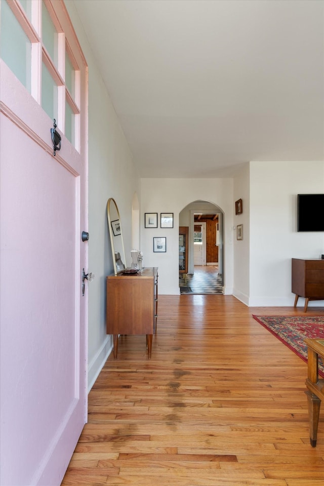 hallway with light wood-type flooring, arched walkways, and baseboards