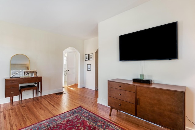 living room featuring arched walkways, baseboards, visible vents, and light wood finished floors