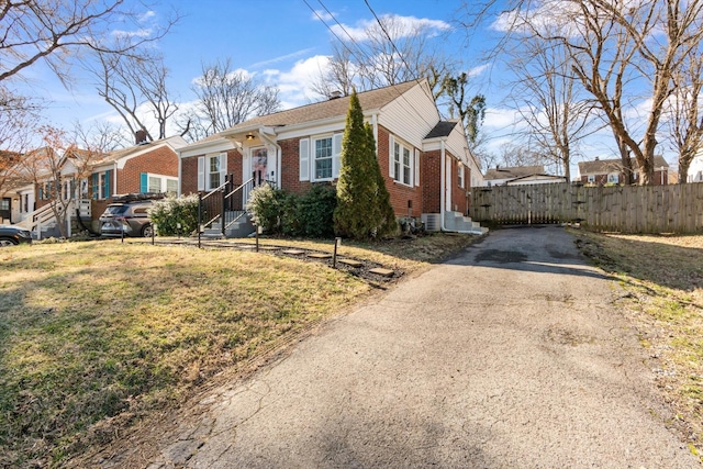 view of front of house with entry steps, aphalt driveway, brick siding, fence, and a front yard