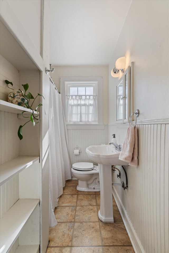 bathroom featuring toilet, stone finish floor, and wainscoting