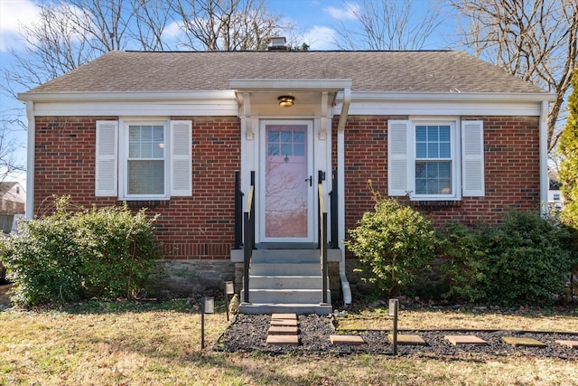 bungalow-style house with entry steps, a shingled roof, and brick siding