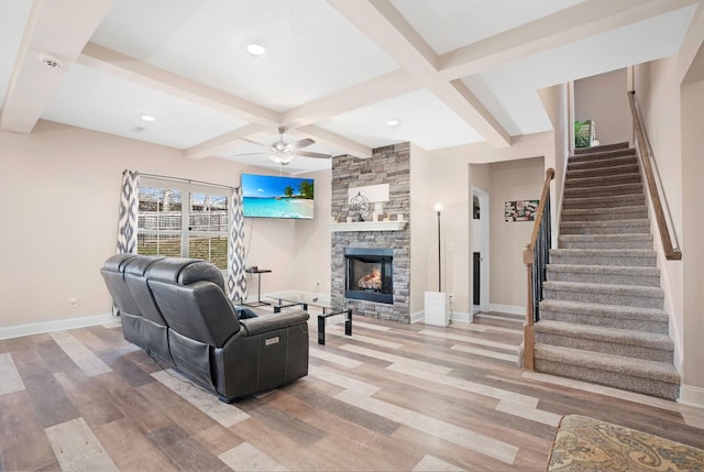 living area featuring baseboards, beamed ceiling, stairs, light wood-type flooring, and a stone fireplace