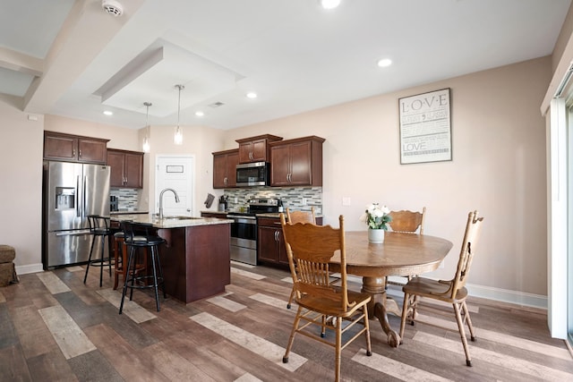 kitchen with a kitchen bar, a kitchen island with sink, a sink, appliances with stainless steel finishes, and dark brown cabinets