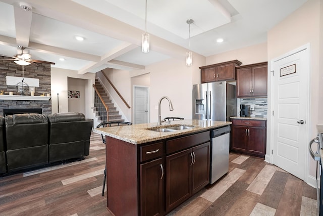 kitchen featuring tasteful backsplash, dark wood-type flooring, a stone fireplace, stainless steel appliances, and a sink