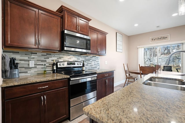 kitchen with light stone counters, baseboards, a sink, decorative backsplash, and stainless steel appliances