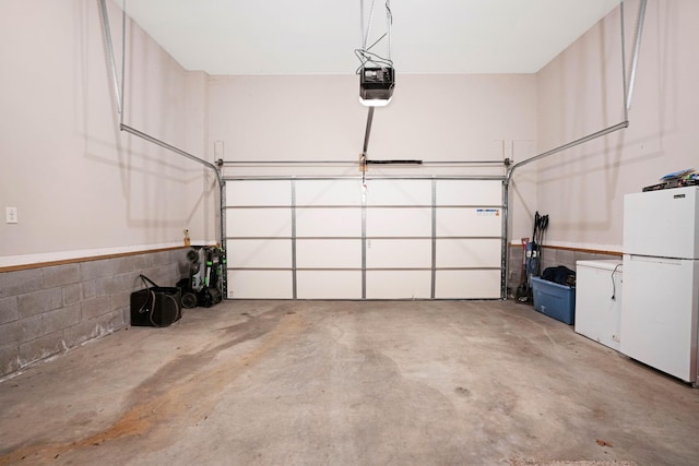 garage with fridge, a garage door opener, concrete block wall, and freestanding refrigerator