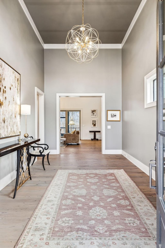 foyer entrance with crown molding, wood finished floors, a towering ceiling, baseboards, and an inviting chandelier