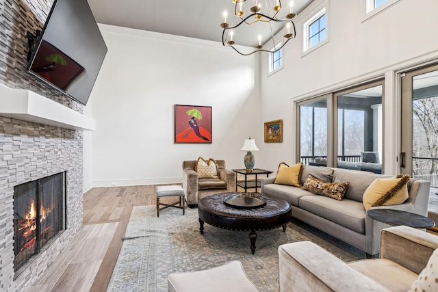 living area with a fireplace, a towering ceiling, a chandelier, light wood-type flooring, and baseboards